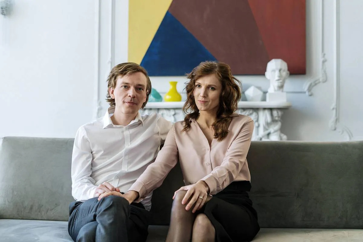 Ein Paar sitzt eng nebeneinander auf einem Sofa und blickt ruhig nach vorn